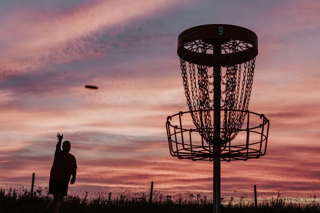 disc golfer putting at a basket at sunset