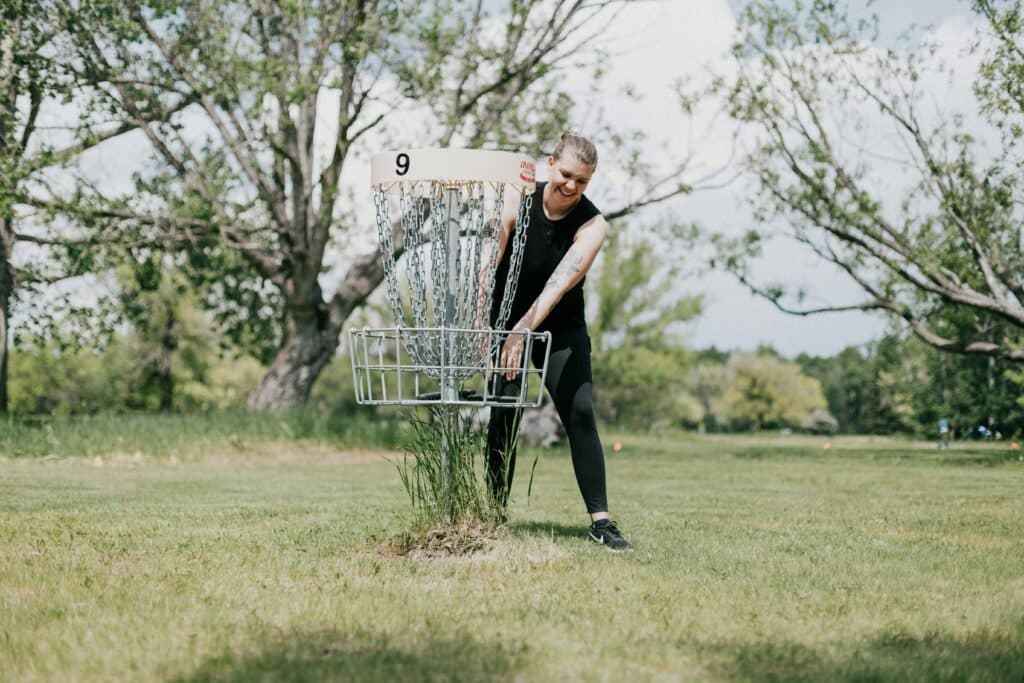A disc golfer getting a disc out of a basket