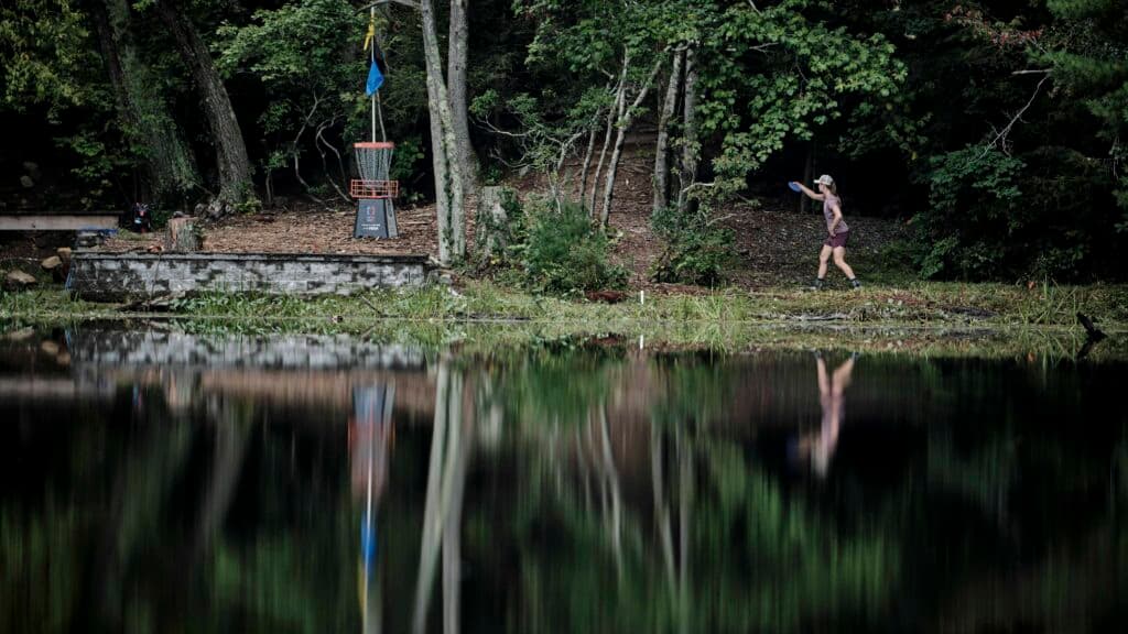 A disc golfer putting near a body of water