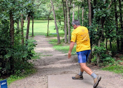 Disc golfer throwing through a tight gap of trees with a straight throw